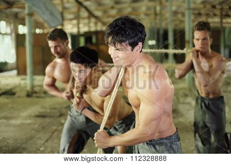Four young guys are dragging something ropes in abandoned building man in the foreground in focus 