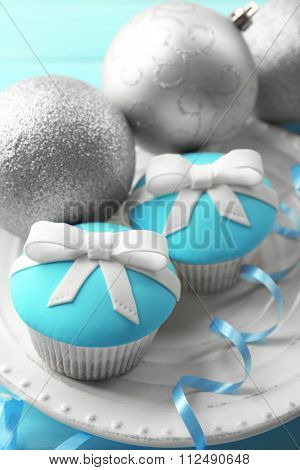 Tasty cupcakes with bow and Christmas toys on color wooden background