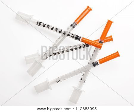 Five plastic syringes with needles closed by protective caps