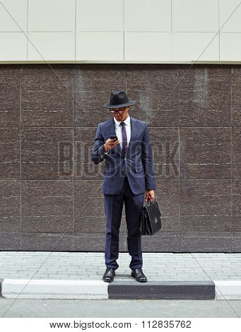Elegant businessman standing on trottoire and using cellphone