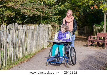 Disability a disabled child in a wheelchair relaxing outside together with a care assistant