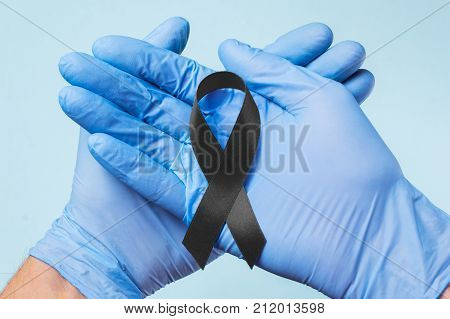 Black Ribbon symbolic color raising awareness on Melanoma and skin cancer prevention and world peace mourning. The doctor's hand in gloves