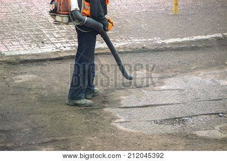 Worker On A Street In Autumn Collects Leaves With A Leaf Blower