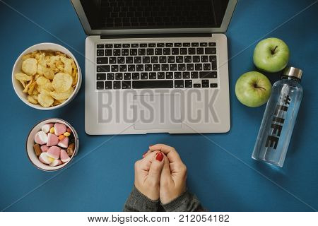 Work space with laptop candy chips water and apple on blue background. Top view space for text
