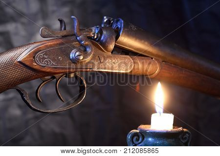 Ancient hunting shotgun closeup near lighting candle on dark background