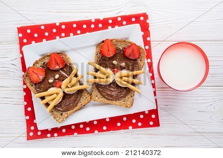 Sandwiches and milk for children's breakfast. Funny cats face sandwiches with berry chocolate banana nuts. Top view