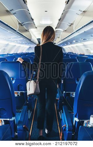Back view of young woman wearing formal suit walking the aisle on plane.