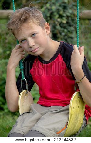 Sad pre-teen boy sitting on a swing outside