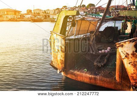 The back side of a fishing an old trawler moored in a harbor with the glow of the sun in the corner