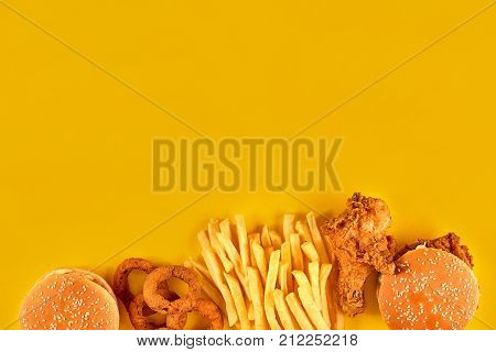 Fast food dish on yellow background. Fast food set fried chicken, meat burger and french fries. Take away fast food. Top view. Copy space. Still life. Flat lay.