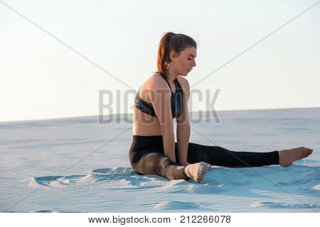Fitness yoga woman stretching on sand. Fit female athlete doing yoga pose before running training outside in amazing landscape.