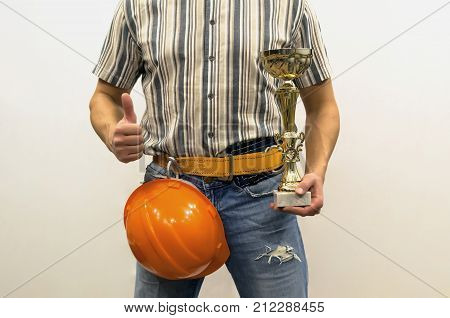 Builder construction worker in mounting belt and with helmet holding in hands golden cup award trophy. Awards ceremony. Best builder worker of the year. Success in construction and repair.