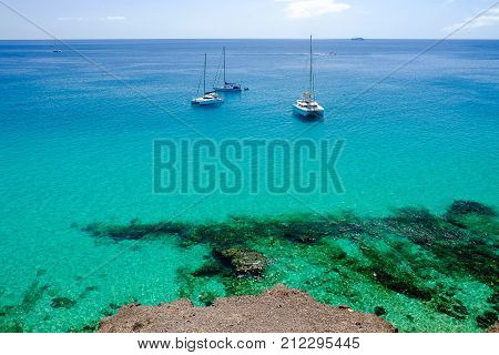 View on the ocean with crystal water and three woutistic boats in Morro Jable on the Canary island Fuerteventura Spain.
