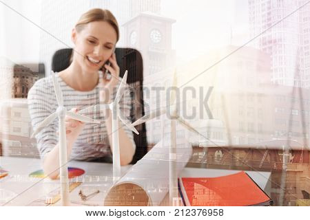 Sustainable energy. Selective focus of wind turbines models standing on the table while a professioanl female engineer sitting in the background and talking on phone