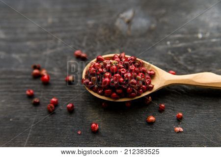 Close up wooden spoon with pink peppercorn on dark background