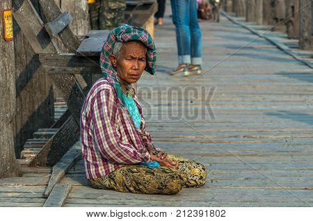 MANDALAY MYANMAR - MARCH 13 : Unidentified Old woman sitting at the ubein bridge on March 13 2016 in Mandalay Myanmar. The U-Bein bridge is the longest teak bridge in the world 1.2km length.