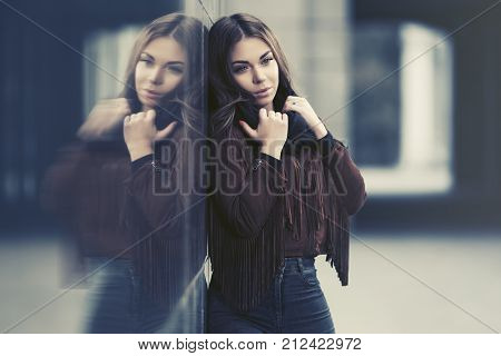 Sad young woman standing at the wall in city street Stylish fashion model in a fringe leather suede jacket 