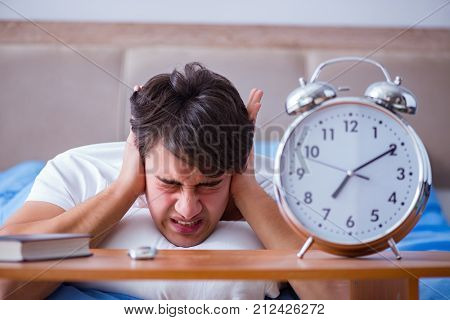 Man in bed frustrated suffering from insomnia with an alarm cloc