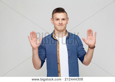 Hands Up. Young Boy Wearing White Tshirt And Blue Shirt Looking At Camera And Give Up