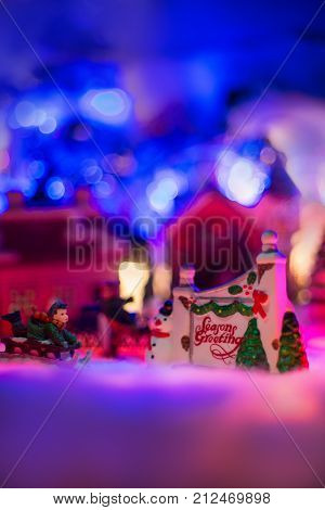 seasons greeting with kid playing sled on snow in snowy christmas village. Winter miniature landscape