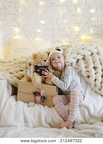 Young baby girl sitting dreaming near magical New year craft gifts by a Christmas tree on yellow magic lights background