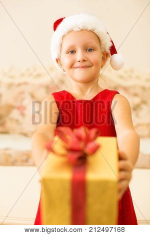 Pleased kind girl giving Christmas gift and looking at camera. Happy kid enjoying gift-giving tradition. Culture concept