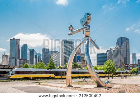 Giant statue walking in Dallas Texas on sunny day with blue sky and blurring train in background