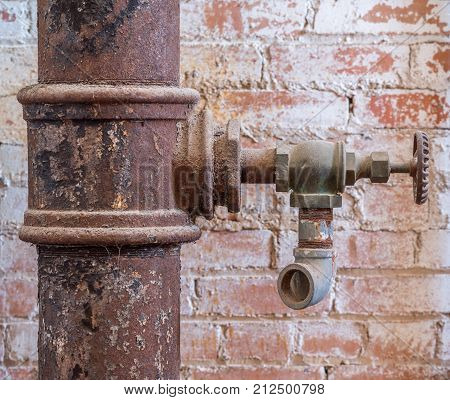 Old faucet and rusty pipe against textured red brick wall.