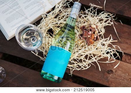 Glasswine with white wine, bottle and pieces of chocolate lies on sawdust near big open book, romantic background with expensive alcoholic drink