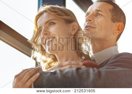 Happy relationships. Nice pleasant caring man standing behind his girlfriend and hugging her while expressing his feelings