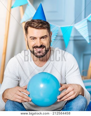 Best party organizer. Cheerful handsome man sitting on the floor and posing with a balloon while organizing a birthday party