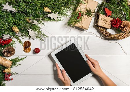 Juniper branches with a Christmas decor. Christmas, New Year background. Coniferous branches of juniper and white tablet with black screen. Top view, flat design. Christmas tree on white wooden background.