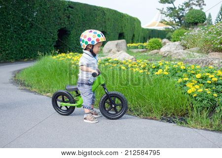 Cute little Asian 1 years / 18 months old baby boy child wearing safety helmet learning to ride first balance bike in sunny summer day kid playing & cycling at park Child first experience concept