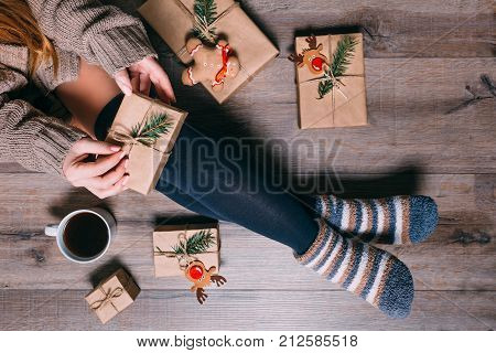 A woman sitting on the floor wrapping presents and drinking coffee at Christmas time. Top view.