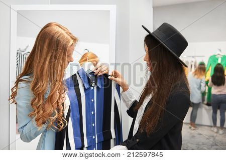 Professional shop assistant showing her female client a new dress in stock. Young stylish woman shopping at the mall service communication advice people lifestyle purchasing salesperson sale discount.