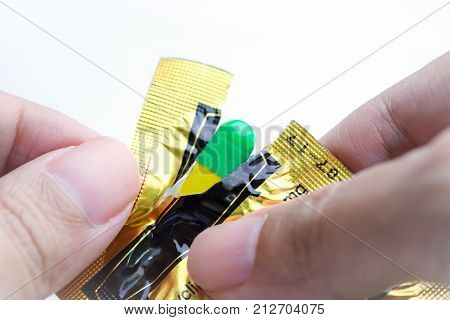 Hands tearing blister pack of green and yellow capsule medical pill.