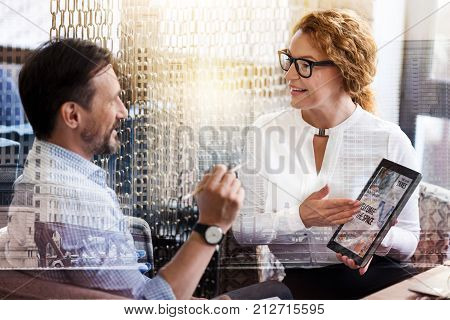 Exchanging information. Beautiful young woman showing the tablet with a news article to her male colleague and discussing it with him