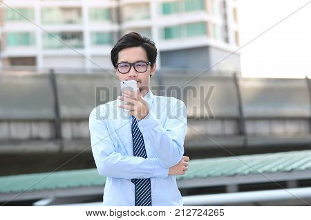 Portrait of confident young Asian business man looking mobile smart phone at outside office.