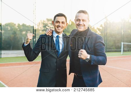 Businessman with hands up. Business Motivation Leadership. Happy Business man. Two business men on tennis court smiling showing teeth. Successful project. Two cheerful business people in formal wear.