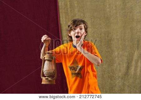 Surprised young actor holds kerosene lamp and places one hand on face