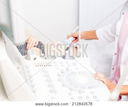 Sonographer scanning young pregnant woman's belly with ultrasonic transducer doing obstetric ultrasonography, focus on a probe