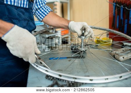 Repairman with handtools checking parts of bicycle wheel
