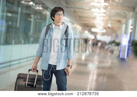 Young Asian man dressed in casual style walking with suitcase luggage in the international airport terminal travel lifestyle concepts