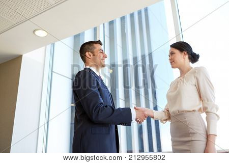 business, partnership and people concept - smiling man and woman shaking hands at office