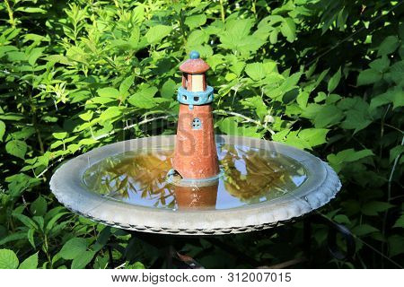 Ceramic Pastel Painted Lighthouse Sitting In The Middle Of A Concrete Birdbath.