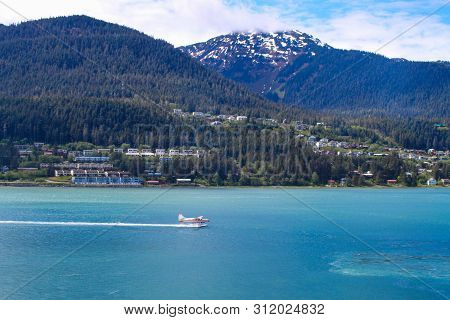 A Seaplane Landing In The Blue Water Near A Small City In Alaska.