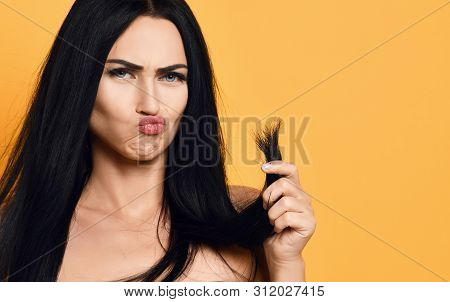 Frustrated Brunette Woman Examining Dry Damaged Hair Over Yellow Background