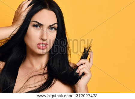 Frustrated Brunette Woman Examining Dry Damaged Hair Over Yellow Background