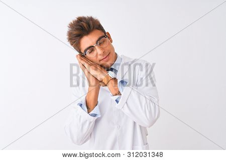 Young handsome sciencist man wearing glasses and coat over isolated white background sleeping tired dreaming and posing with hands together while smiling with closed eyes.