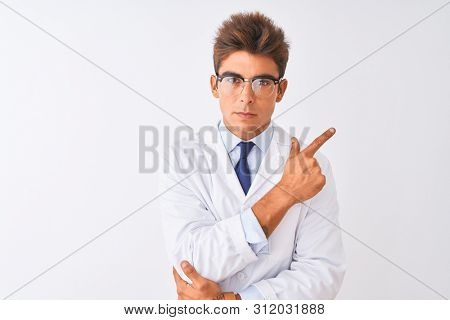 Young handsome sciencist man wearing glasses and coat over isolated white background Pointing with hand finger to the side showing advertisement, serious and calm face